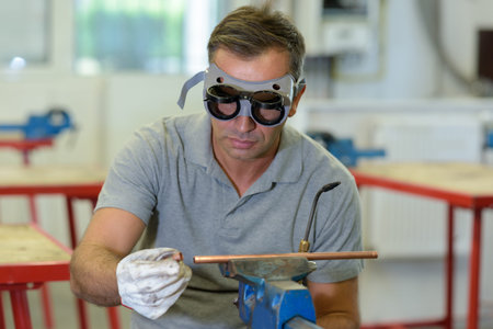 man wearing goggles preparing copper pipe for welding