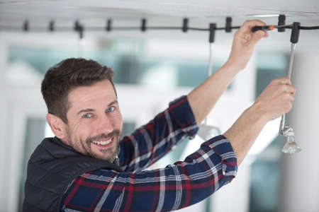 happy male electrician is repairing ceiling lightの写真素材