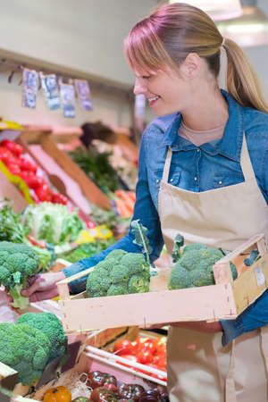sales assistant restocking broccoli in green grocersの写真素材