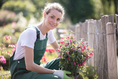 young woman holding a potted pink flower plant in gardenの写真素材
