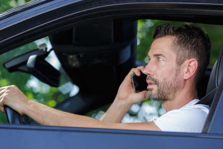 man driving car while using mobile phoneの写真素材