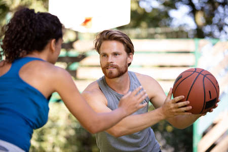 beautiful couple flirting and playing on an asphalt basketball courtの写真素材