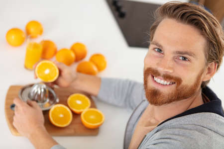 attractive young man preparing orange juiceの写真素材