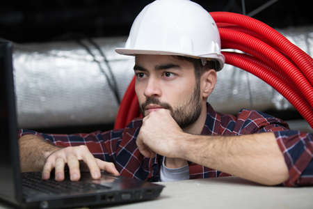 tradesman in roof space using a laptopの写真素材