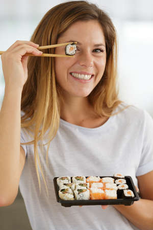 smiling young woman holding sushi in front of eyeの写真素材