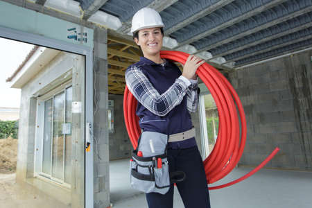 female-worker holding a reel of red pipe on her shoulderの写真素材