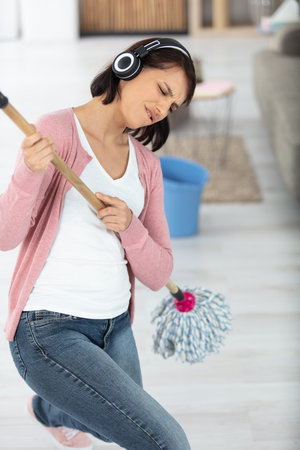 beautiful young woman is dancing and smiling while cleaning floor