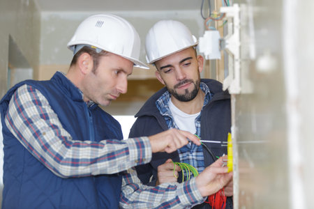 two workers screwing electric terminal to wall