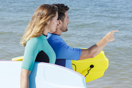 couple with boogie boards checking out the wavesの写真素材