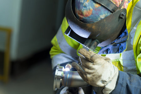 worker wearing visor welding metal pipe