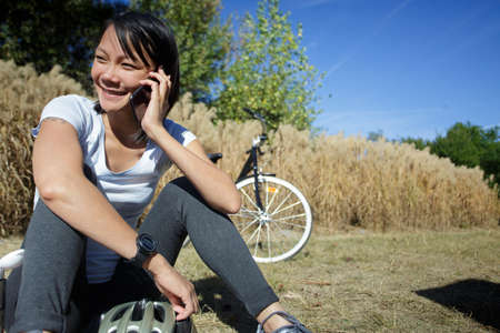 young lovely girl sitting on grass and talking on cellphoneの写真素材
