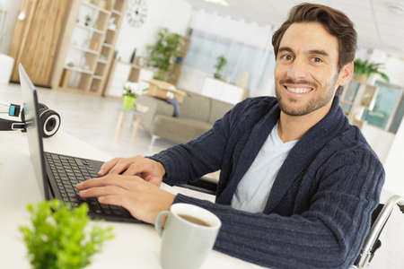 portrait of man in wheelchair using laptop at homeの写真素材