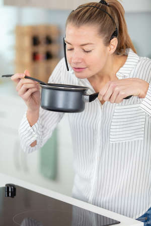 lady smelling food in saucepan while wearing handsfree headsetの写真素材
