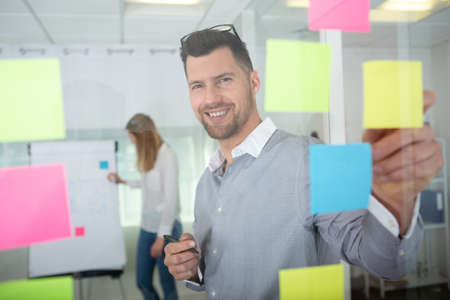 happy creative team writing on stickers at office glass boardの写真素材