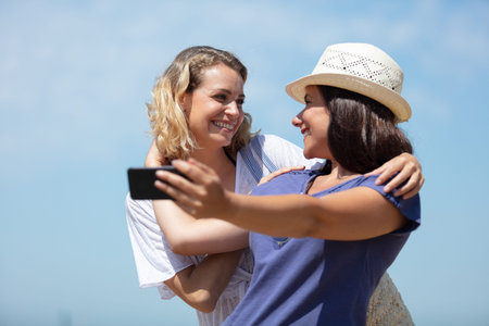 happy girlfriends taking selfie against blue sky