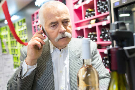 senior man choosing wine while using the phoneの写真素材