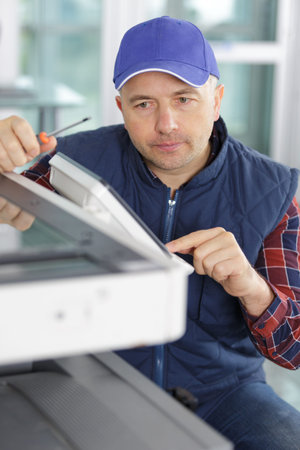 man leaning over open photocopier during maintenance repairs