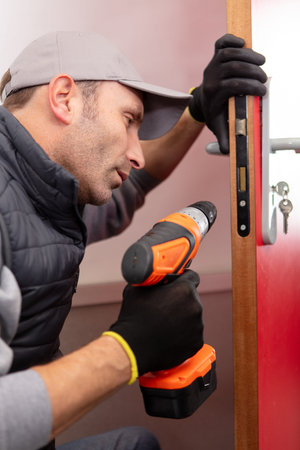 young contractor using cordless drill on door lockの写真素材