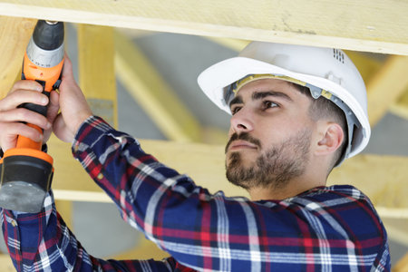 young builder working on wooden roof joist
