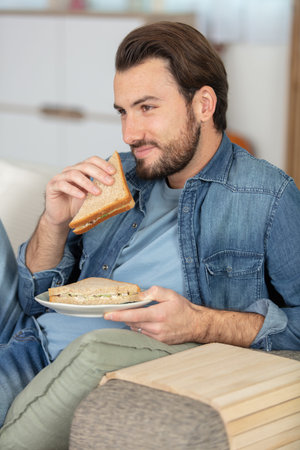 young man eating sandwich on his sofa