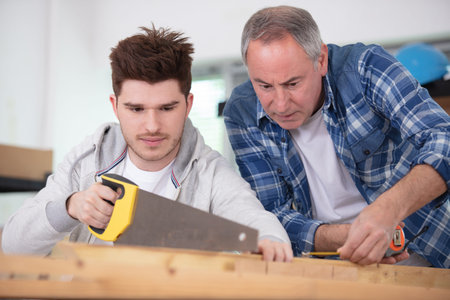 experienced male teacher of carpentry skill acquaints a teenager