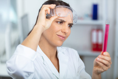 female scientist lifting goggles to inspect test tube