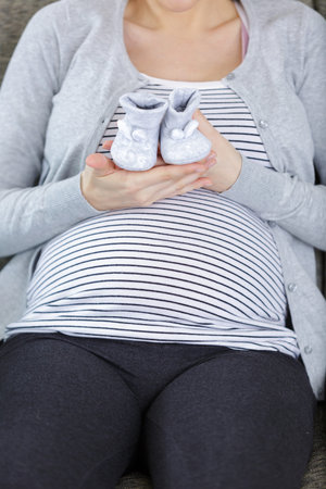 beautiful pregnant woman with baby boots on color background