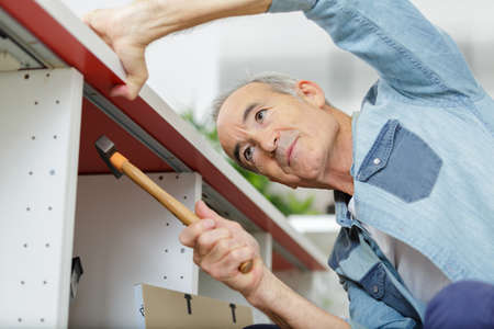 senior man using hammer to fit kitchen cupboardの写真素材