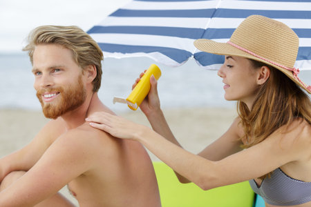 lady applying suncream to her partners back on beach