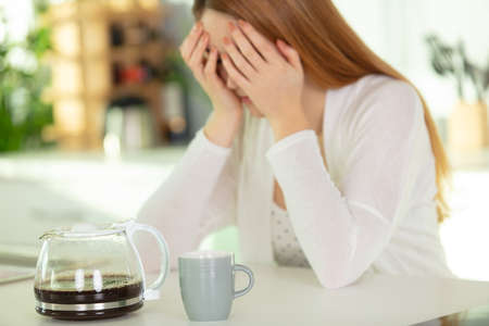 woman with a coffee holding her head in her handsの写真素材