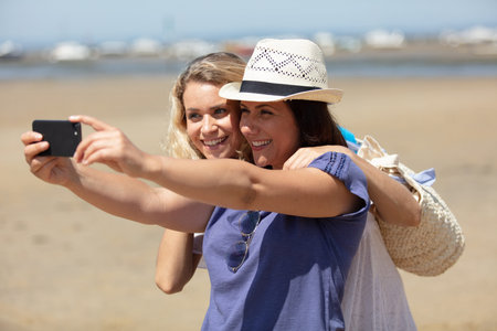 female friends taking selfies on the beach with a smartphone