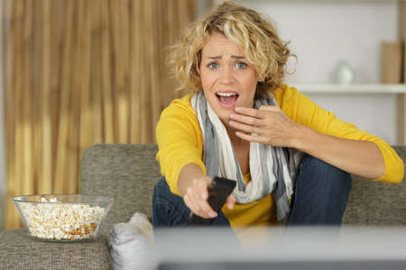 shocked woman at home on the couch watching tvの写真素材
