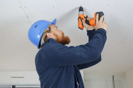 worker using a cordless drill on a plasterboard ceilingの写真素材