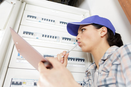 woman electrician inspecting fuseboard holding clipboard