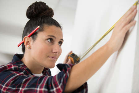 young woman is measuring a wall with measuring tapeの写真素材