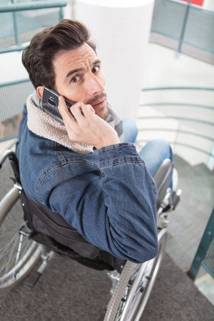 handicapped young man in wheelchair talking by phone at home