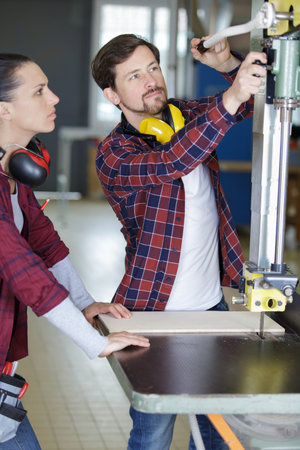 colleagues cutting wood in workshopの写真素材