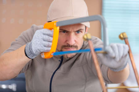 tradesman cutting copper pipe with hacksawの写真素材
