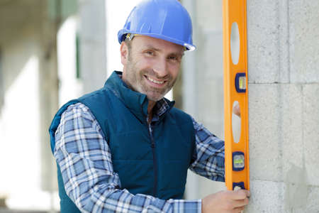 happy worker checks erected brick wall with levelの写真素材