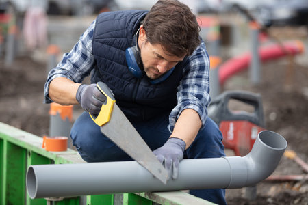 young male plumber sawing through pvc pipe
