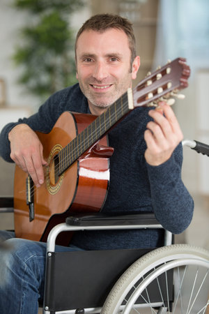 middle aged man in wheelchair tuning guitar