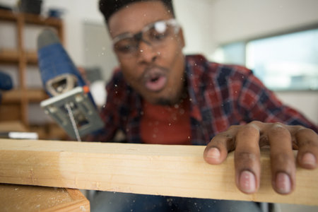 mixed-race carpenter blowing dust from woodの写真素材