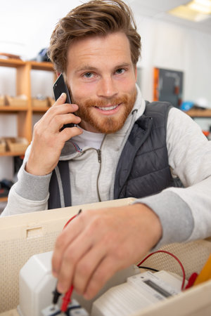 electrician using a multimeter and talking on smartphone