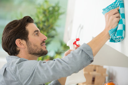 man cleaning kitchen cupboard with cloth and sprayの写真素材
