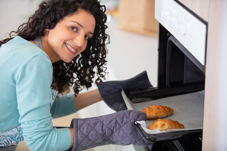 young woman looking at fresh baked croissants in the ovenの写真素材