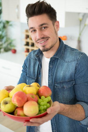 healthy young man holding a bowl of fruitの写真素材