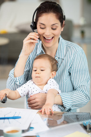 mom holding her newborn while working in home office interiorの写真素材