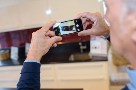 mature man photographing his kitchen with a smartphone