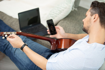 man using a smartphone app to learn guitarの写真素材