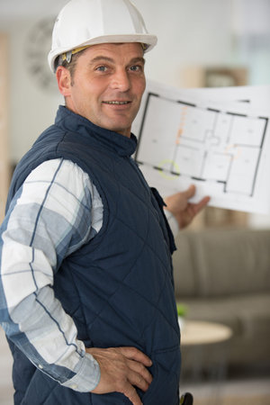 a man in helmet with blueprint showing plan on site